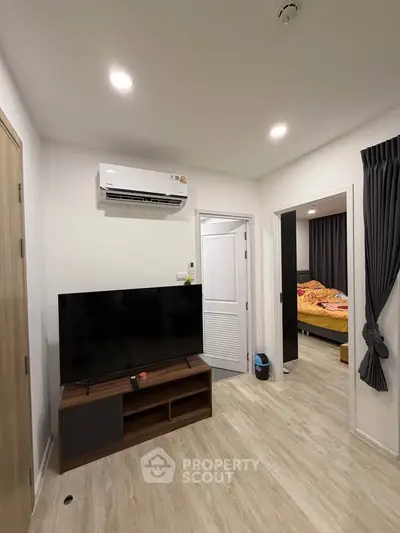 Modern living room with TV and air conditioning, leading to a cozy bedroom.