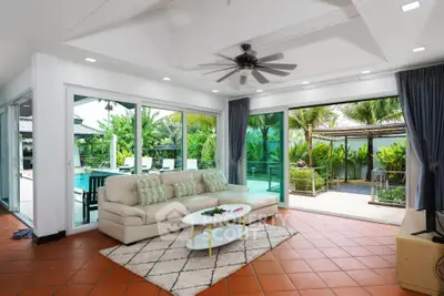 Spacious living room with pool view, modern furniture, and large sliding glass doors opening to lush garden.