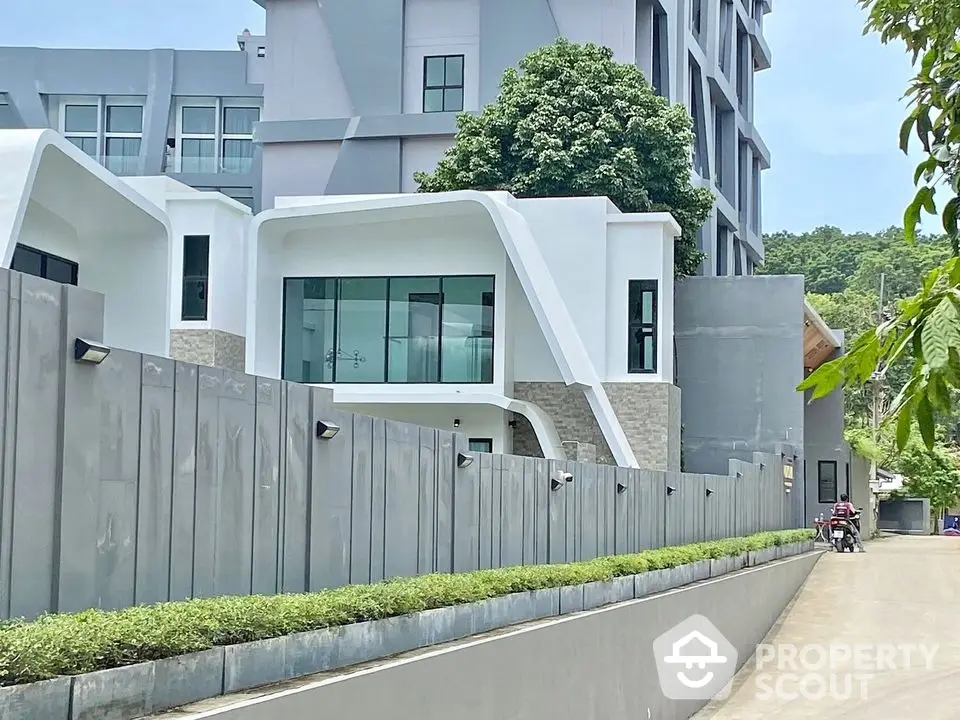 Modern architectural building with sleek design and large windows, surrounded by lush greenery and a secure fence.