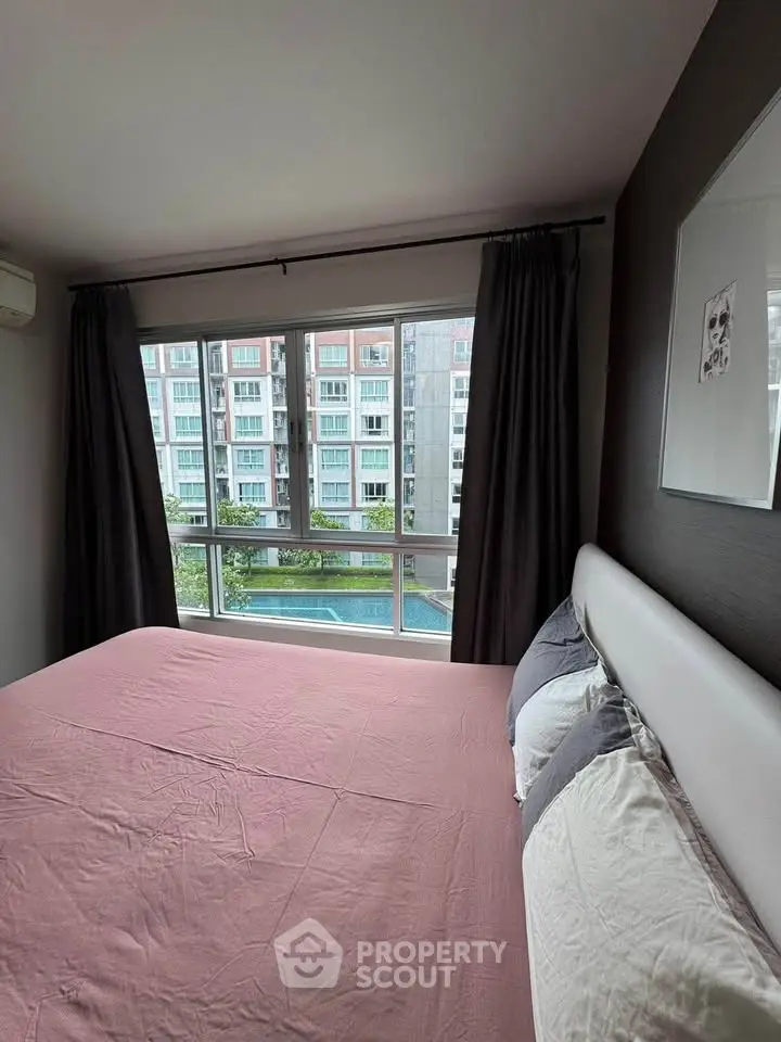 Cozy bedroom with large window offering a view of the pool and neighboring buildings.