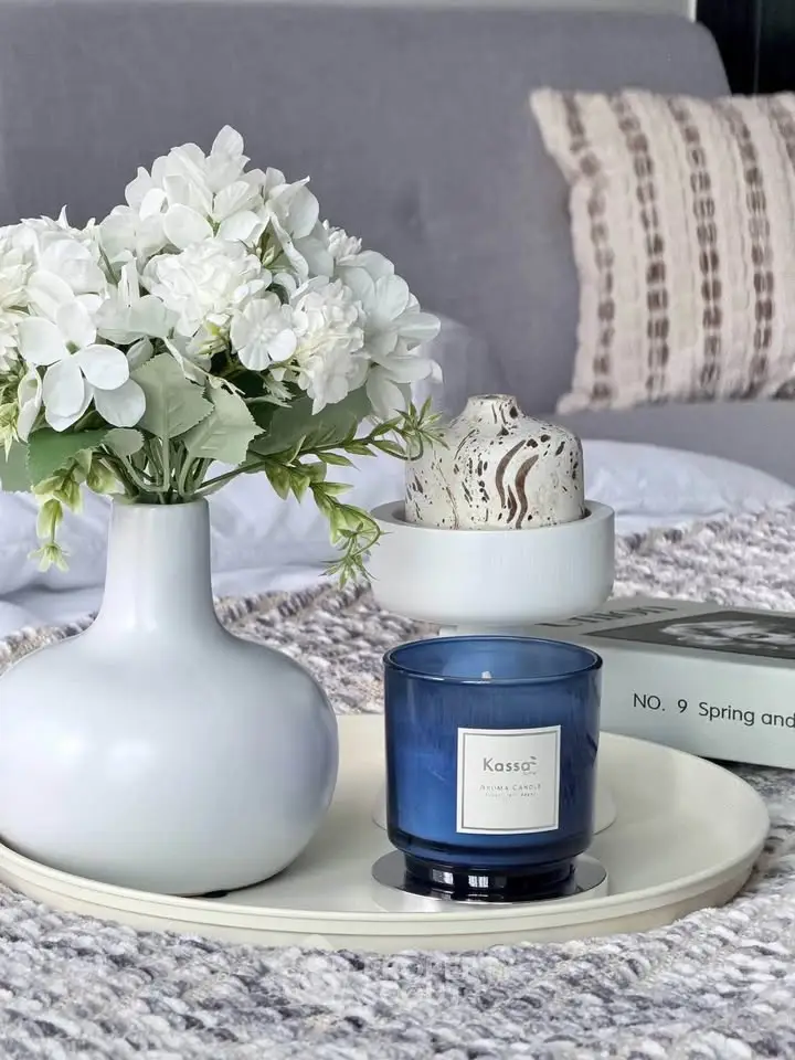 Elegant living room decor with white flowers and blue candle on a tray, enhancing cozy ambiance.