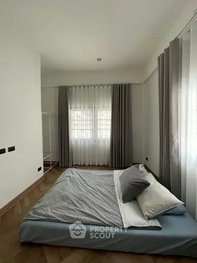 Spacious bedroom with large windows and elegant curtains, featuring a minimalist bed setup.