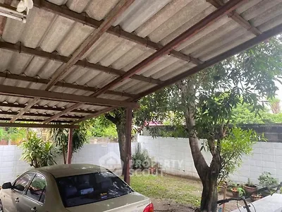 Spacious carport with lush greenery and sturdy roofing in a serene backyard setting.