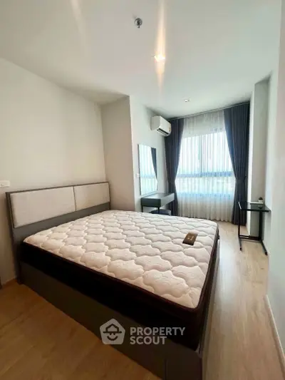 Spacious bedroom with large window and modern furnishings in a stylish apartment.