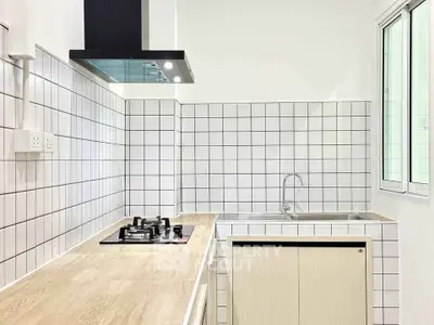 Modern kitchen with sleek gas stove and minimalist design, featuring white tiled backsplash and wooden countertops.
