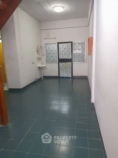 Spacious tiled room with sink and large windows, ideal for versatile use.