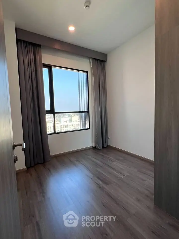 Spacious empty room with large window and wooden flooring, perfect for customization.