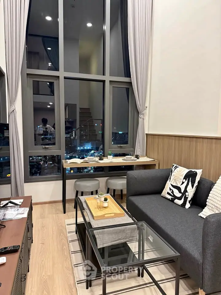 Modern living room with high ceilings and city view, featuring stylish furniture and large windows.