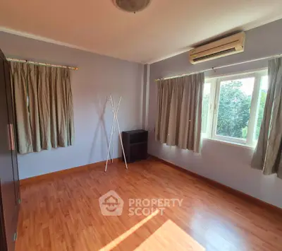 Spacious empty bedroom with wooden flooring and large windows offering natural light.