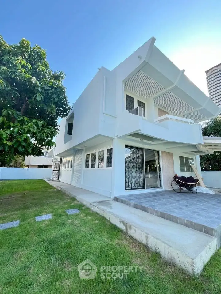 Modern white two-story house with lush green lawn and spacious patio.