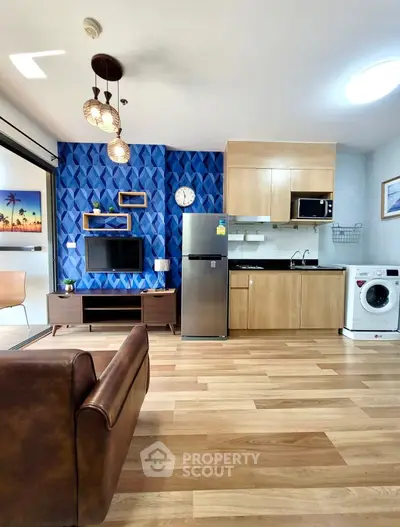 Modern living room with stylish decor, featuring a kitchen area with appliances and vibrant blue accent wall.