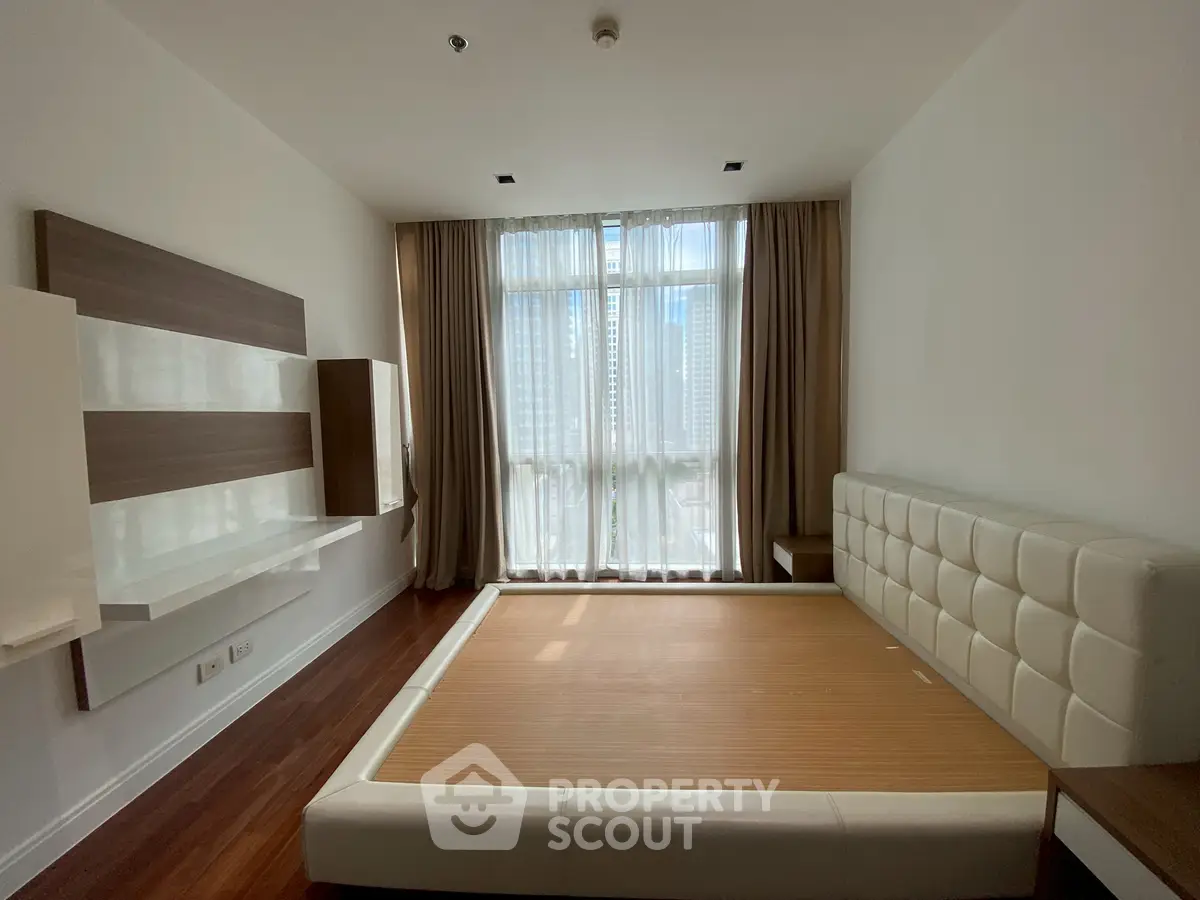 Spacious bedroom with large window and modern design in a high-rise apartment.