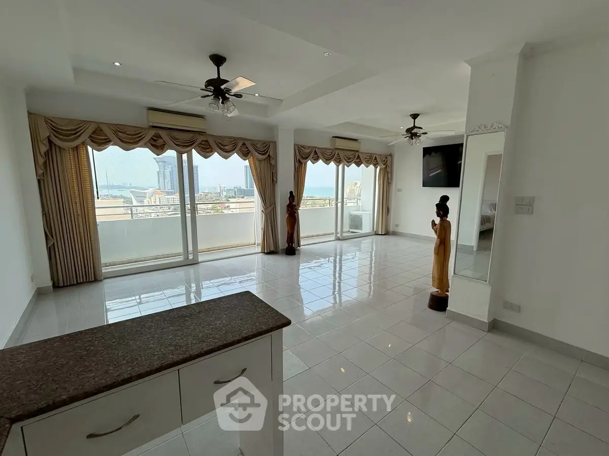 Spacious living room with large windows and city view, featuring elegant decor and ceiling fans.