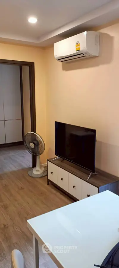 Modern living room with air conditioning and TV, featuring stylish wooden flooring and neutral walls.
