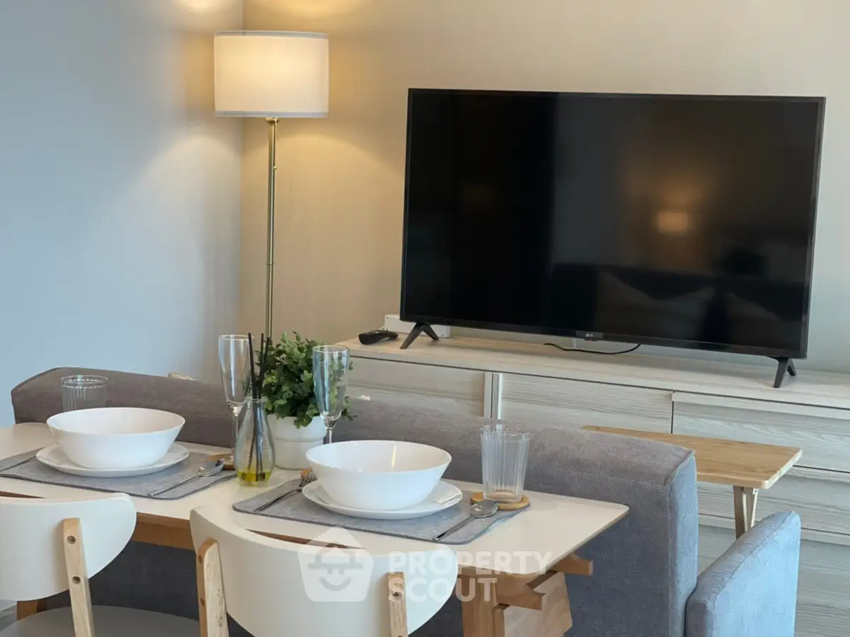 Modern minimalist dining area seamlessly integrates with cozy living space, featuring sleek furnishings and a large flat-screen TV, perfect for urban living.
