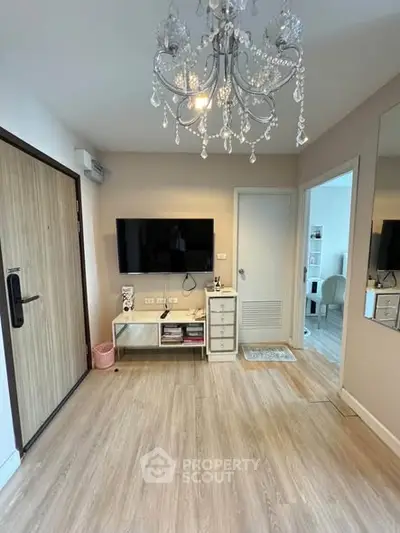 Modern living room with elegant chandelier and wall-mounted TV in stylish apartment.