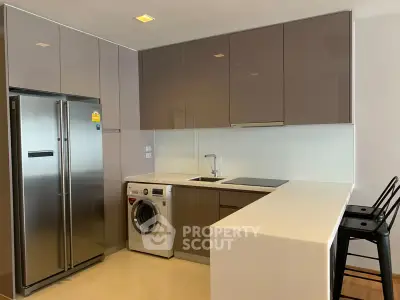 Modern kitchen with sleek cabinets, stainless steel fridge, and washing machine in open layout.