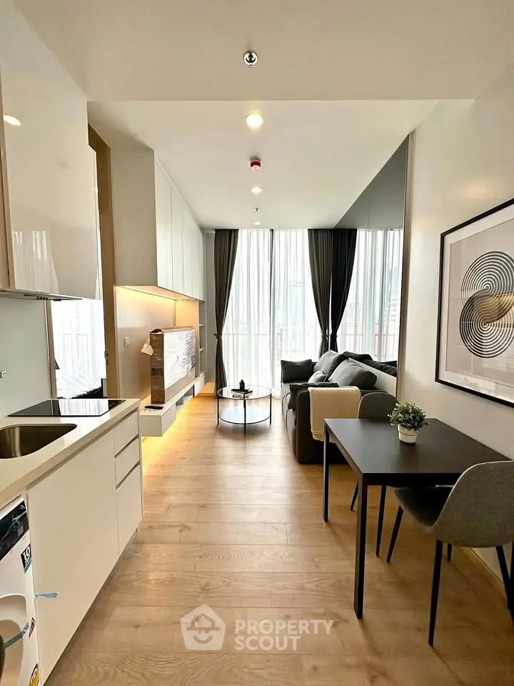 Modern living room with open kitchen, stylish decor, and large windows for natural light.
