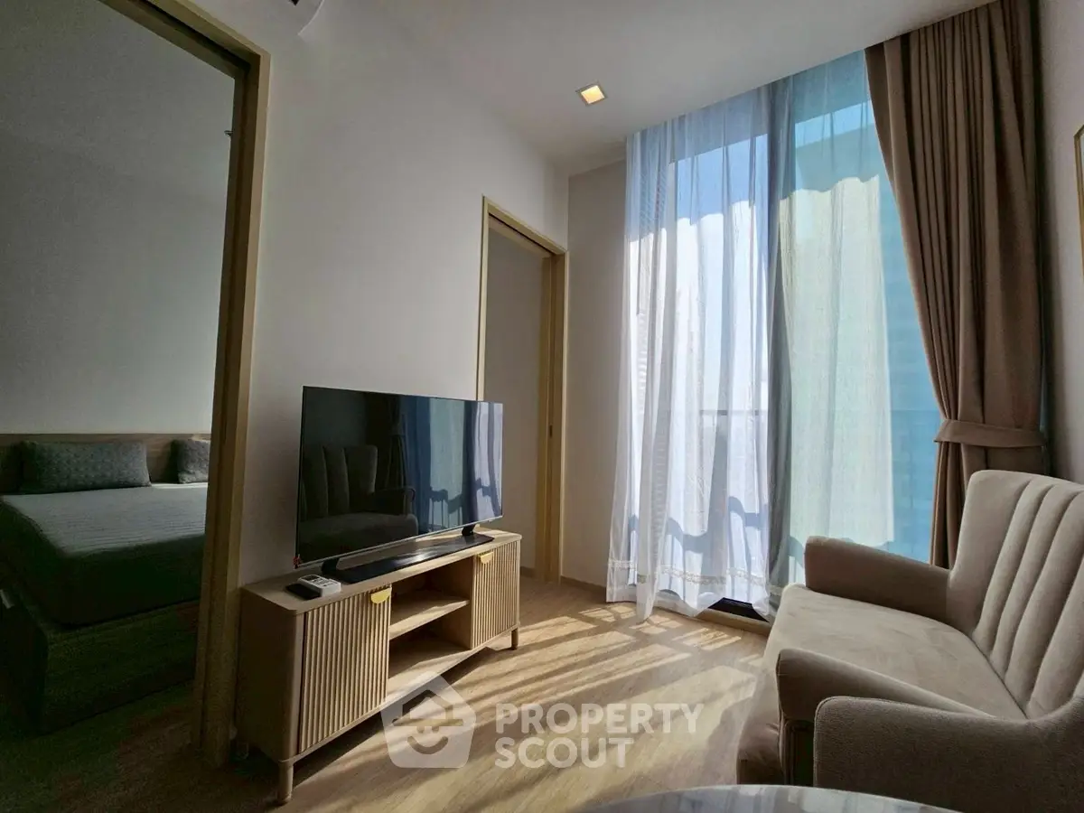 Modern living room with natural light, sleek furniture, and a view of the bedroom.