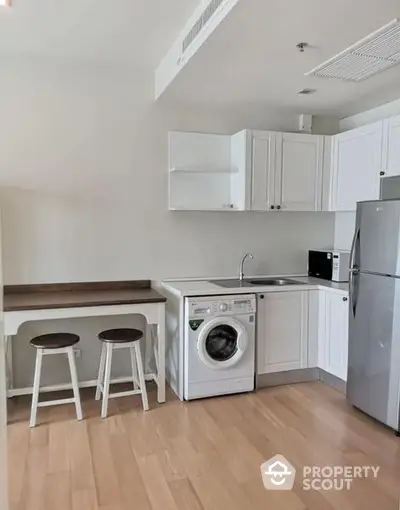 Compact modern kitchen with built-in appliances, sleek white cabinetry, and a convenient washing machine, perfect for urban living.