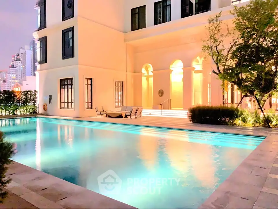 Luxurious apartment building with illuminated pool and elegant architecture at night.