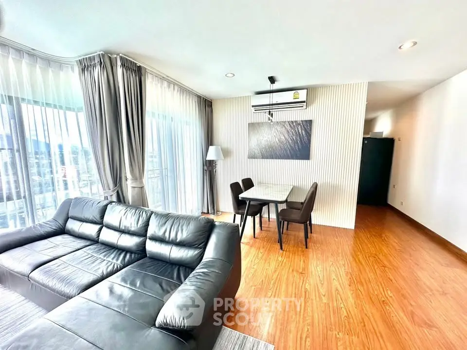 Spacious modern living room with leather sofa and dining area, featuring large windows and wooden flooring.
