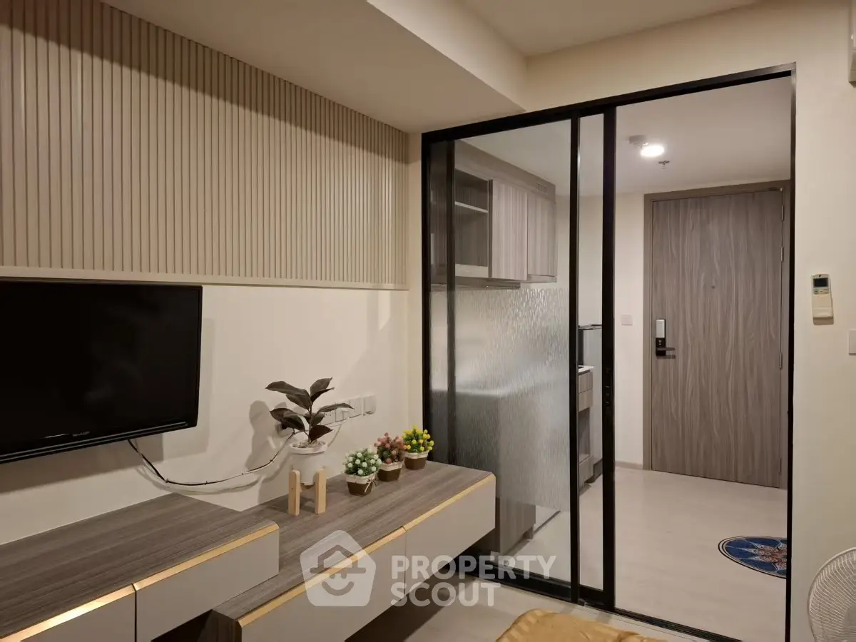 Modern living room with sleek TV unit and glass partition leading to kitchen