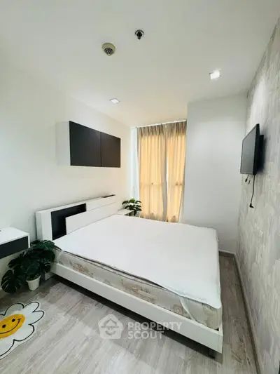 Modern bedroom with minimalist design, featuring a cozy bed, wall-mounted TV, and natural light from large windows.