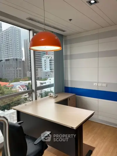 Modern office space with city view, featuring sleek desk and vibrant orange pendant light.