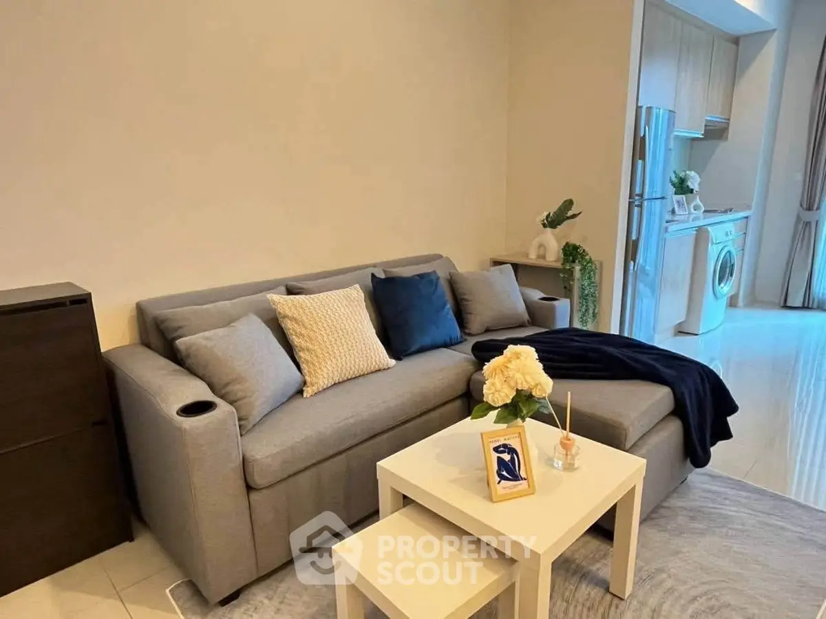 Modern living room with cozy gray sofa and stylish decor, adjacent to sleek kitchen area.