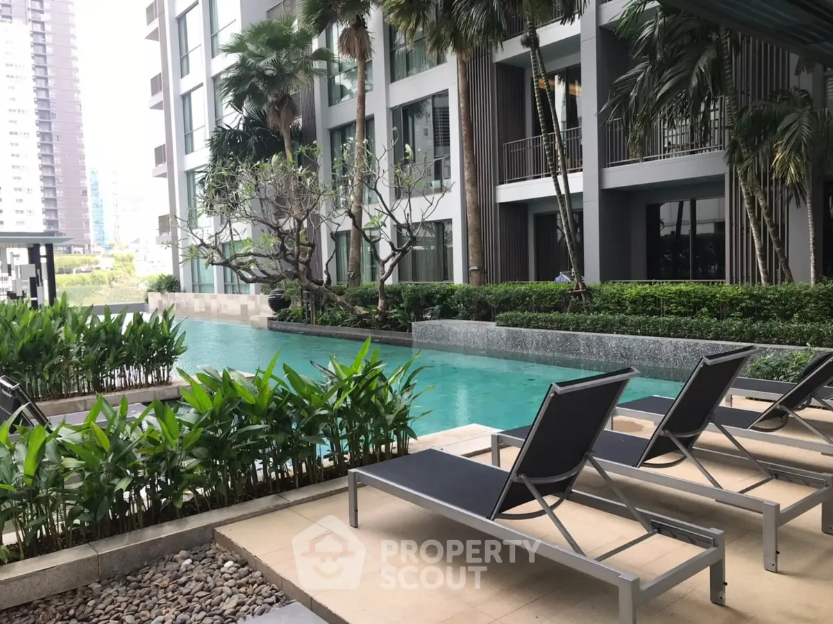 Luxurious condominium pool area with modern lounge chairs and lush greenery