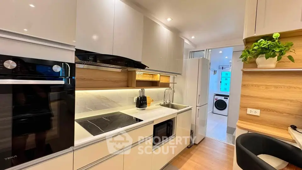 Modern kitchen with sleek appliances and open layout, featuring a view into a laundry area.