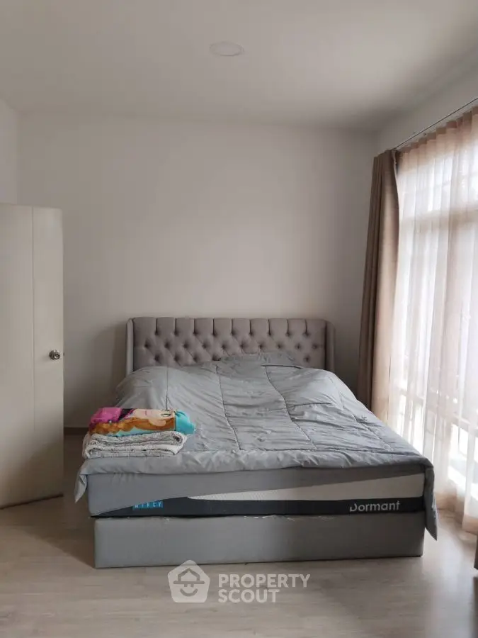 Cozy bedroom with plush bed and natural light through large windows.
