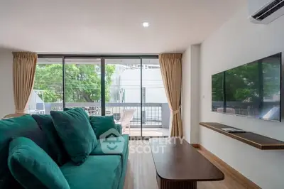 Modern living room with large green sofa and wall-mounted TV, overlooking a spacious balcony.