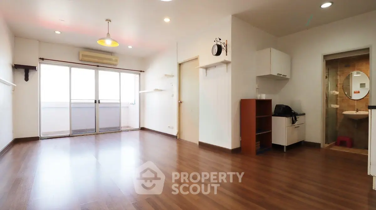 Spacious open-plan living room with wooden flooring and balcony access.