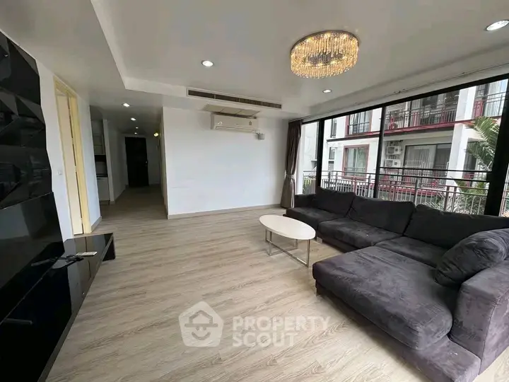 Spacious modern living room with large windows and elegant chandelier in a stylish apartment.