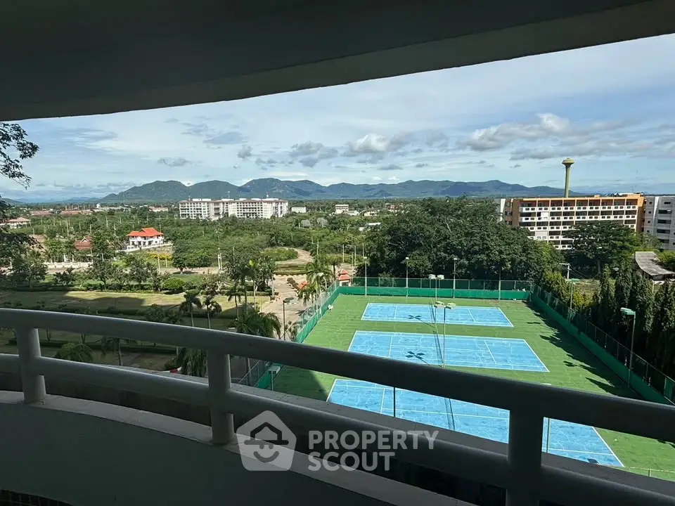 Stunning view from balcony overlooking tennis courts and lush greenery with mountains in the background.
