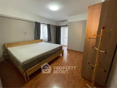 Spacious bedroom with wooden flooring and large windows for natural light.