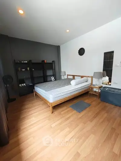 Spacious bedroom with modern decor and wooden flooring, featuring a comfortable bed and stylish shelving.