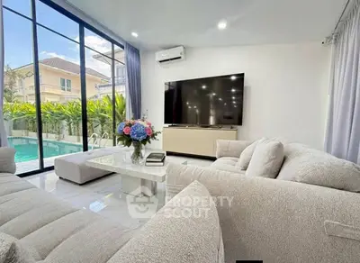 Luxurious living room with pool view, modern furniture, and large TV in a bright, airy space.