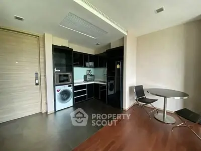 Modern kitchen with sleek black cabinets, washing machine, and dining area in open layout.