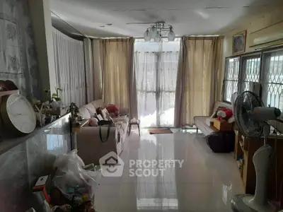 Spacious living room with large windows and elegant curtains, featuring cozy seating and modern decor.