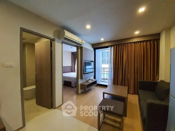 Modern apartment interior with open living room and bedroom, featuring sleek furniture and large windows.