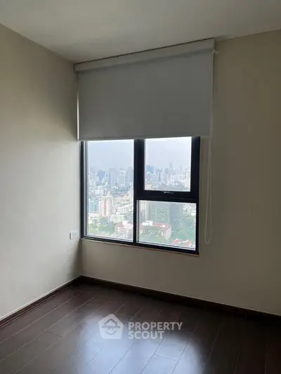 Spacious room with large window offering stunning city skyline view, perfect for urban living.