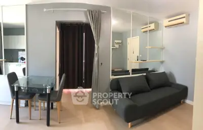 Modern living room with sleek black sofa, glass dining table, and mirrored wall in stylish apartment.