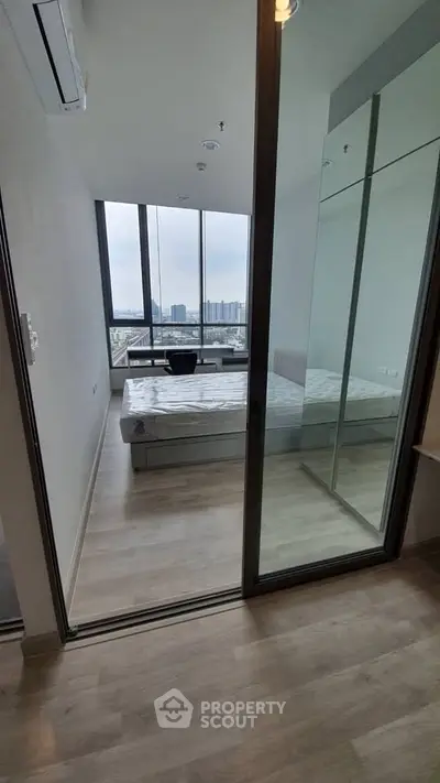 Modern bedroom with floor-to-ceiling windows offering stunning city views, featuring sleek design and ample natural light.
