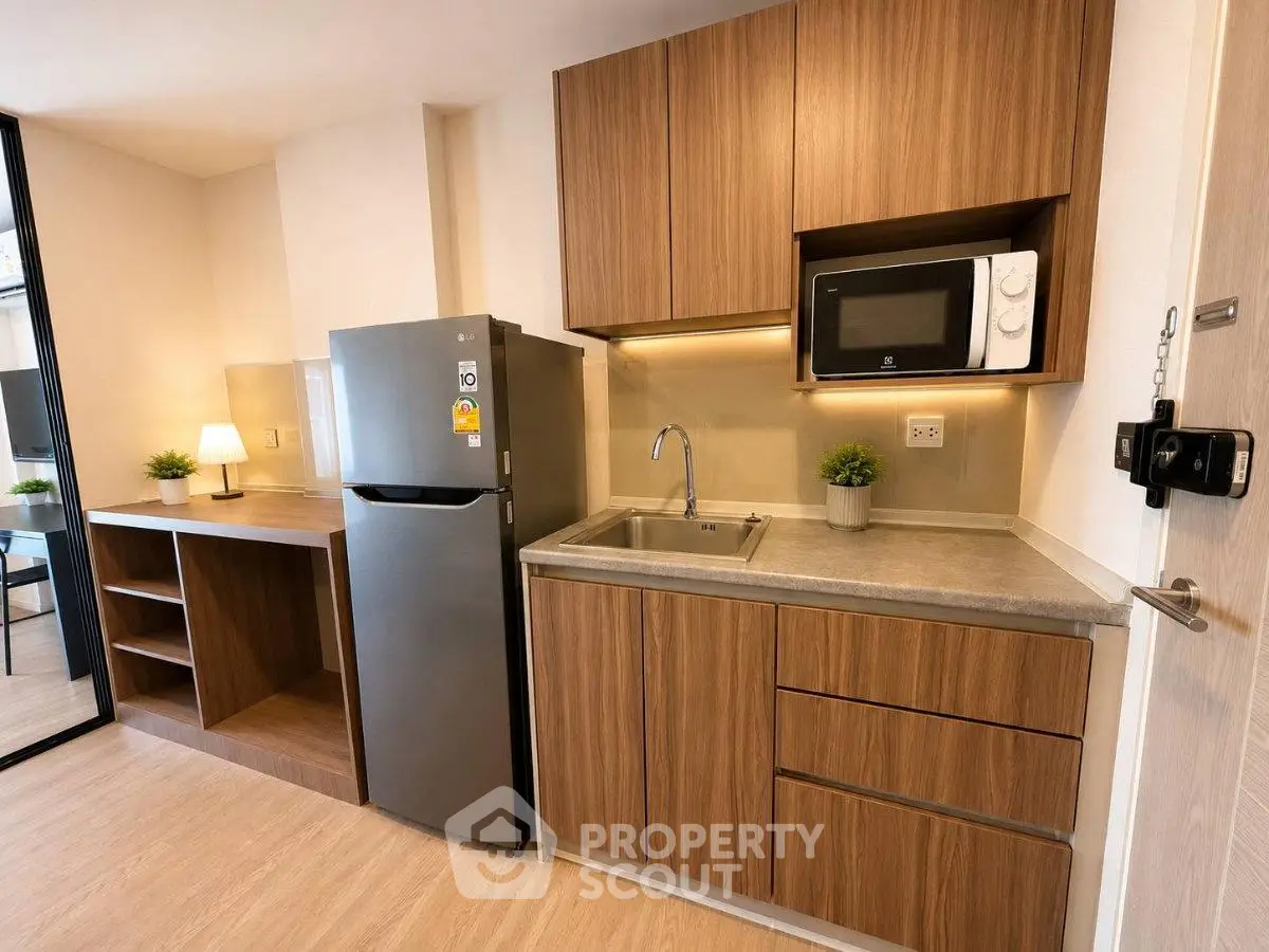 Modern kitchen with sleek wooden cabinets, stainless steel fridge, and microwave in a cozy apartment.