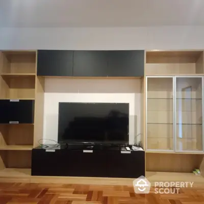 Spacious living room with modern built-in wooden shelving units surrounding a large flat-screen TV, set against a parquet floor.