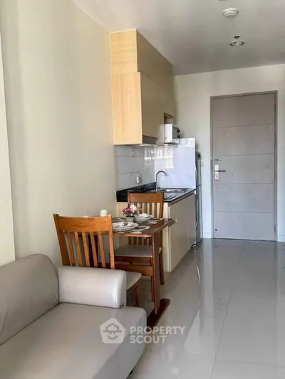 Modern compact kitchen with dining area in a cozy apartment, featuring sleek cabinetry and a comfortable sofa.