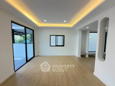Spacious modern living room with wooden flooring and recessed lighting, featuring large windows for natural light.